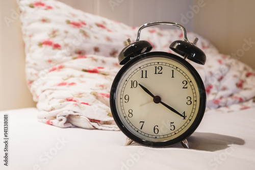 Retro alarm clock with 10 O'clock and twenty minuet, on white bed with pillow