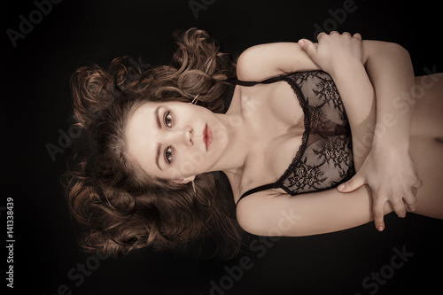 serious girl in lingerie lying on black background