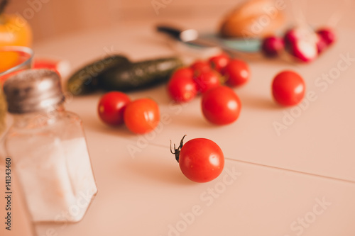 Fresh ripe cherry tomatoes with cucumber and solt on table in kitchen closeup. Selective focus.