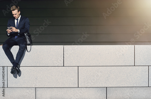 Businessman with phone is sitting on handrail