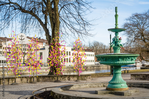 Street view of inactive fountain with traditional colourful feathers on trees for Easter decorations in Uppsala  Sweden  Europe