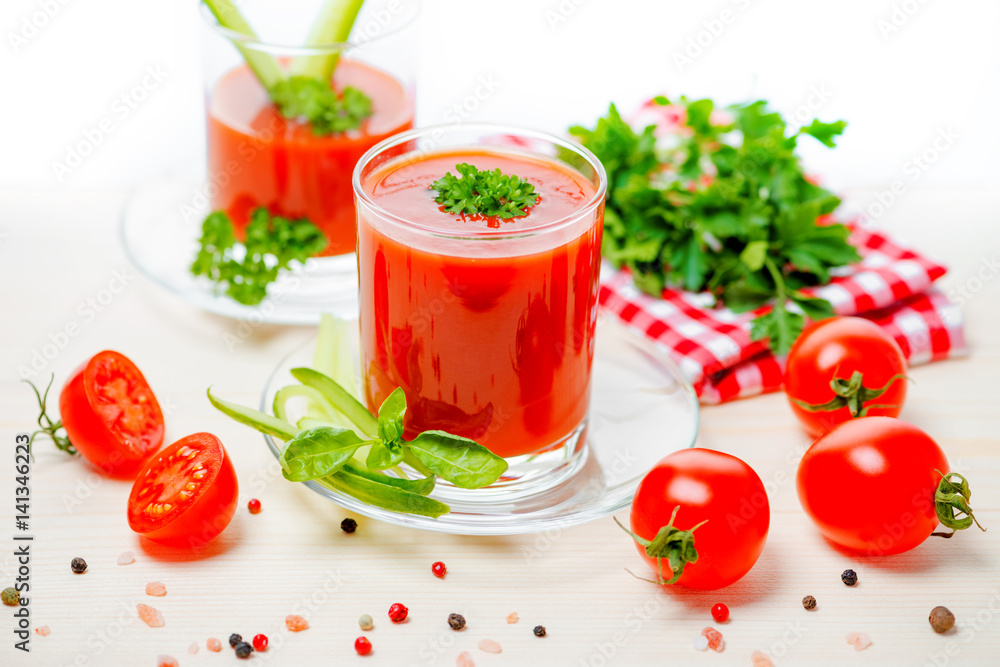 tomato juice in transparent glasses with parsley, basil, cucumber and napkin on light wooden background, concept vegetarian food, close up tomato juice in transparent glasses with parsley, basil, cucumber and napkin on light wooden background, concept vegetarian food, close up
