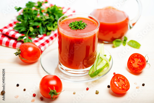 tomato juice in glass, jug with greenery, basil, cutted tomato fruit and dry pepper on light wooden background, concept vegetarian food, close up