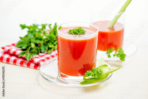 tomato juice in transparent glasses with parsley, cucumber and napkin on light wooden background, close up