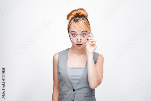 Young fair-haired woman looks shocked, speechless and perplexed. Confused, surprised and dumbfounded blonde on grey background.