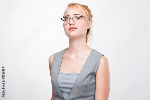 Young blonde woman looks shocked, stunned, taken aback and perplexed. Dumbfounded and bemused girl on grey background.