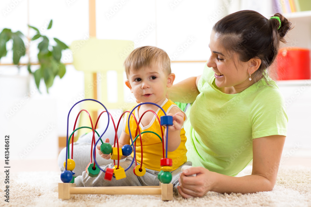 Kid boy plays with educational toy in nursery at home. Happy mother looking at her smart son. Kid boy plays with educational toy in nursery at home. Happy mother looking at her smart son.