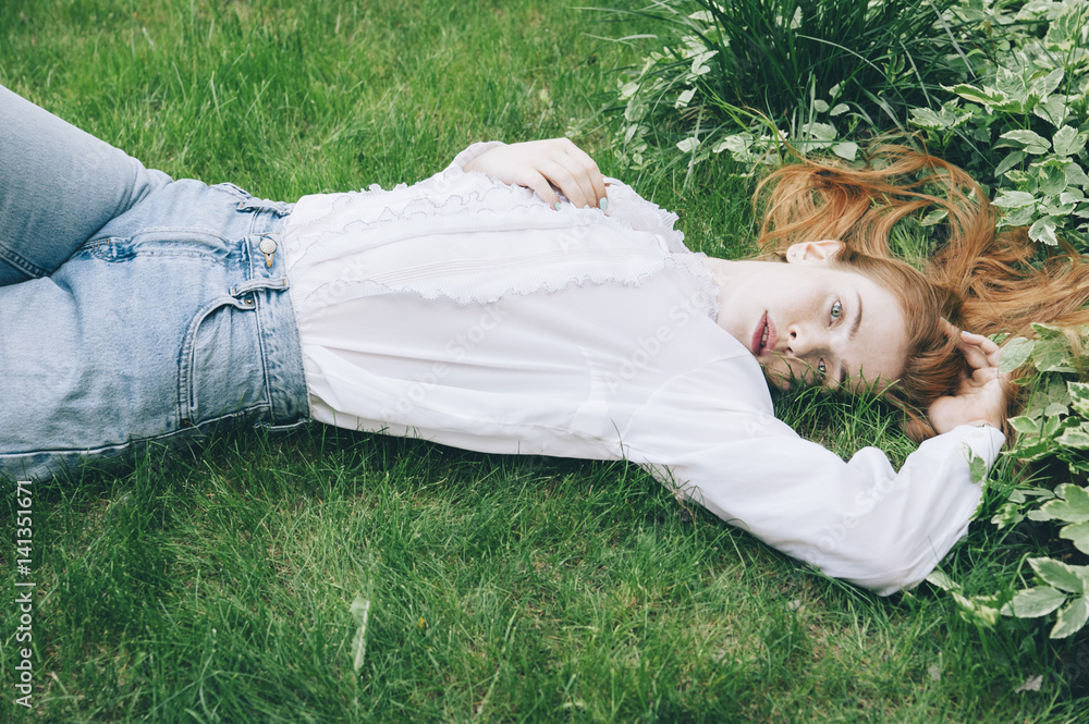 Stunning redhead woman lying on the summer green grass sleepily looking to the camera Stunning redhead woman lying on the summer green grass sleepily looking to the camera