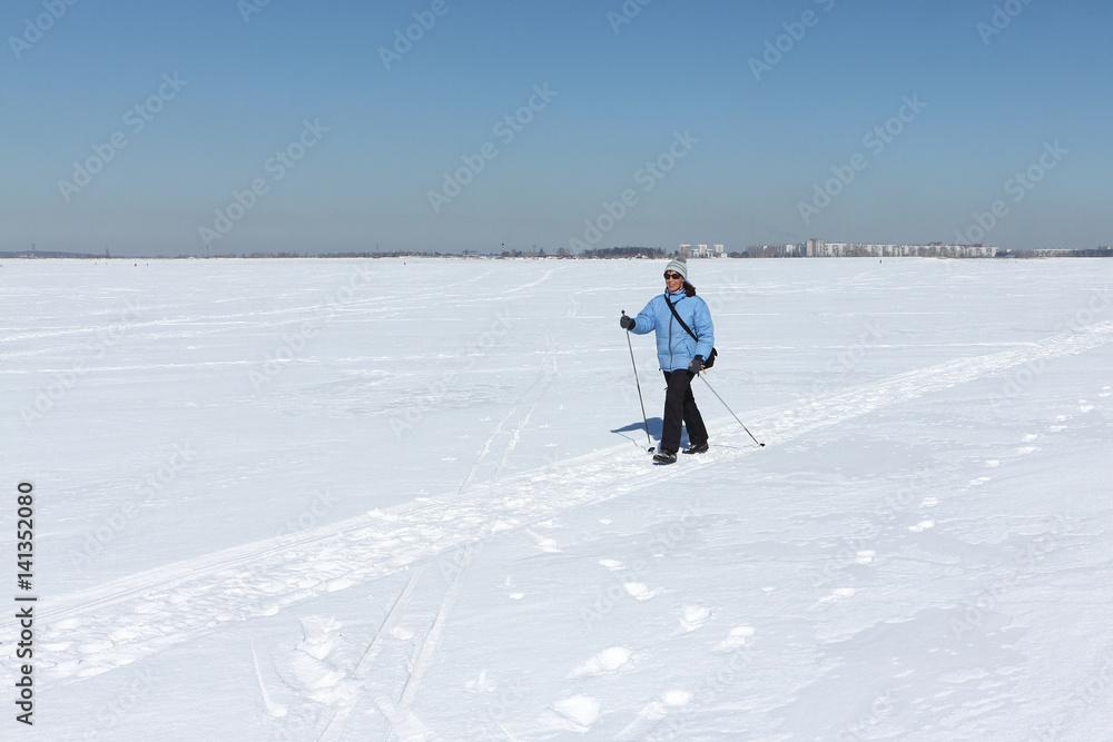 Nordic Walking - adult woman in a blue jacket hiking on snow