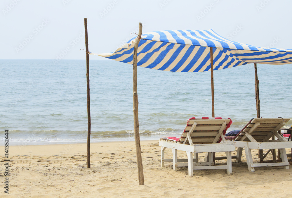 Two chaise lounges under a canopy on the beach near the ocean