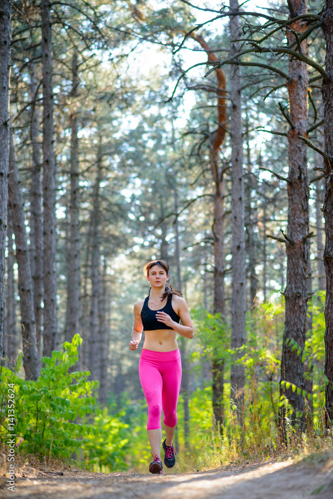 Young Woman Running on the Trail in the Beautiful Wild Pine Forest. Active Lifestyle Concept. Space for Text.