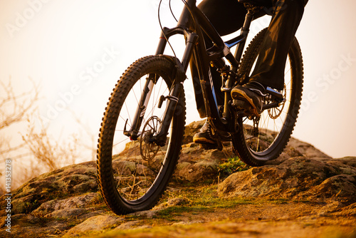 Enduro Cyclist Riding the Bike Down Rocky Hill at Sunset. Close up Extreme Sport Concept. Space for Text.