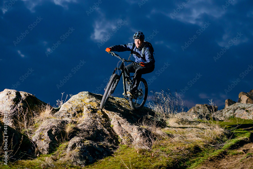 Enduro Cyclist Riding the Bike on the Rock at Night. Extreme Sport Concept. Space for Text.