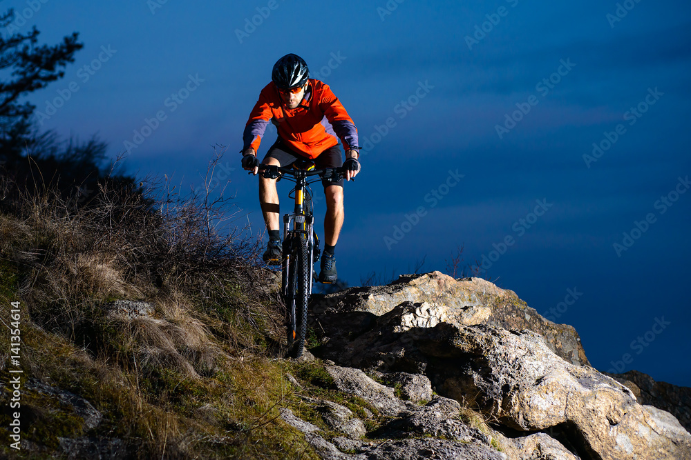 Enduro Cyclist Riding the Bike on the Rock at Night. Extreme Sport Concept. Space for Text.