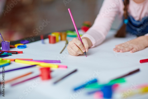 Little girl holding crayon or highlighter on paper
