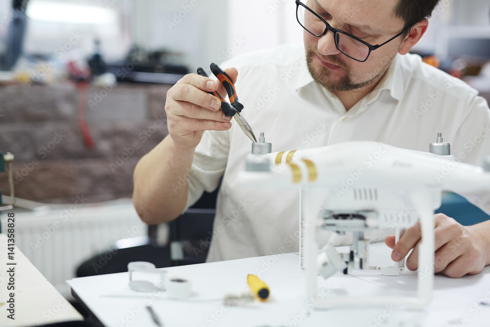 Portrait of modern man working on repairing tech, assembling drone on white table with assorted tools in workshop Portrait of modern man working on repairing tech, assembling drone on white table with assorted tools in workshop