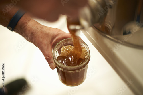 Hands of female beekeeper pouring honey into jar from kitchen vat