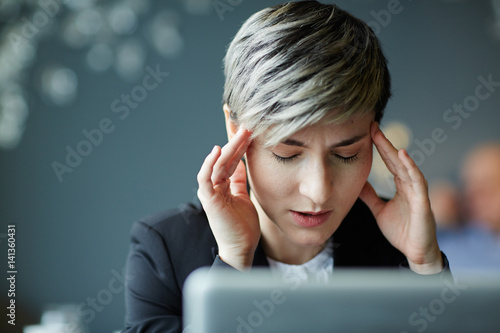Portrait of young businesswoman with closed eyes suffering from headache while working on laptop in modern office