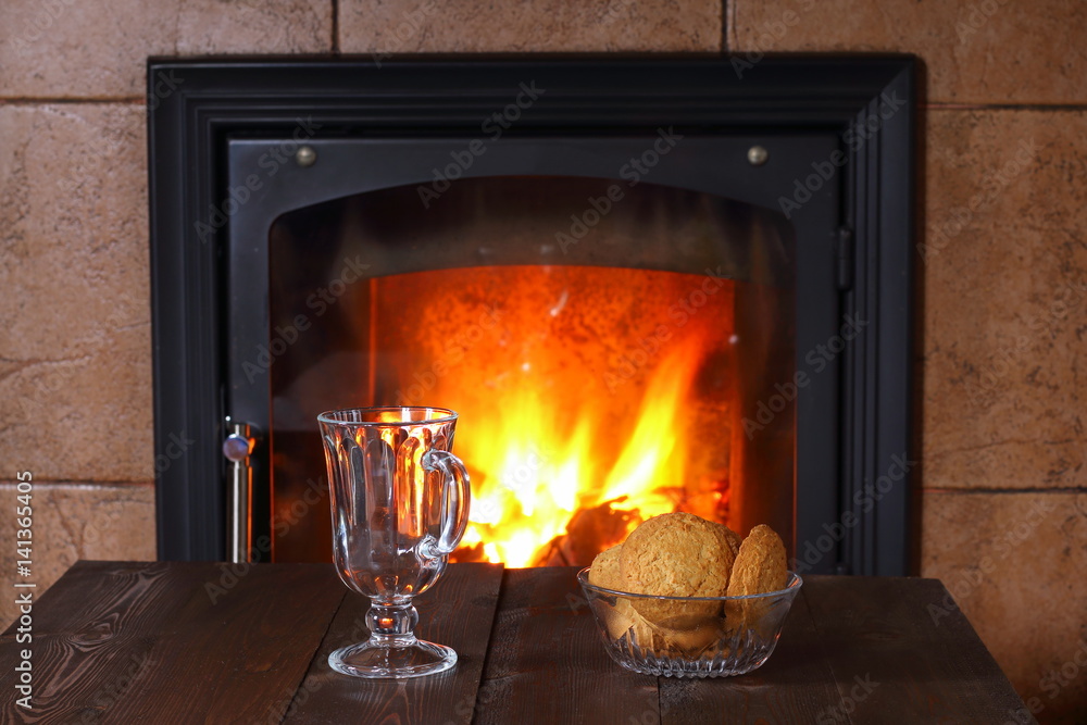 A glass for tea and a vase with biscuits are on the table in front of the fireplace. A glass for tea and a vase with biscuits are on the table in front of the fireplace.