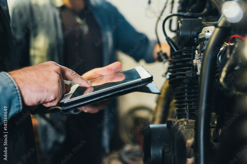 Two mature men, working in garage, using digital tablet, close-up Two mature men, working in garage, using digital tablet, close-up