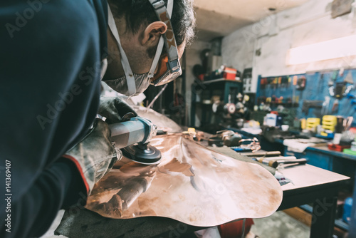 Metalworker polishing copper in forge workshop photo
