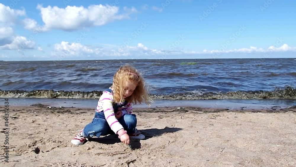 Beautiful little girl sitting writes some signs on a seaside sand Beautiful little girl sitting writes some signs on a seaside sand