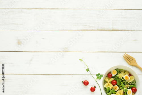 Light summer meal concept. Green salad with pasta  cherry tomato  quail eggs on a white table. Copy space.