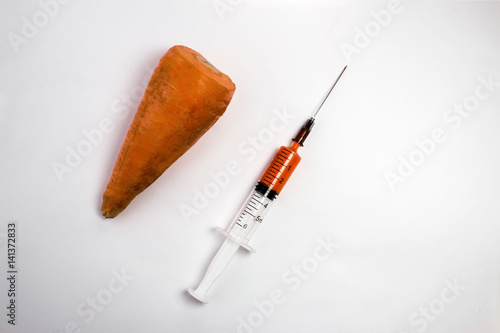 Genetically modified organism - ripe carrot with syringes and laboratory glassware on white background