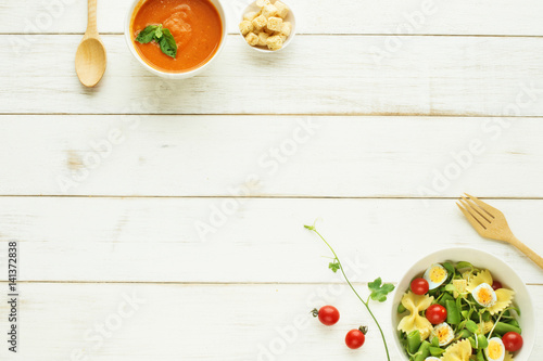 Light summer meal concept. Green salad with pasta, cherry tomato, quail eggs. Cold tomato soup (gazpacho) with croutons on a white table. Copy space. 