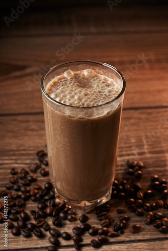 Coffee and banana smoothie in a glass on a wooden background