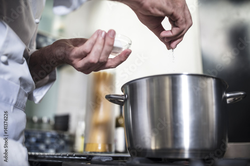 Chef putting salt in pan of water on stove, close-up photo