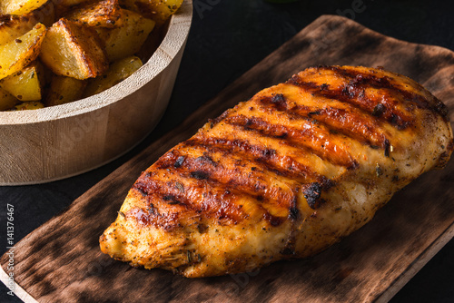 Grilled chicken breast on wooden board and grilled potato