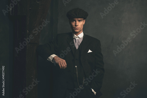 Retro 1920s english gangster wearing suit and flat cap.