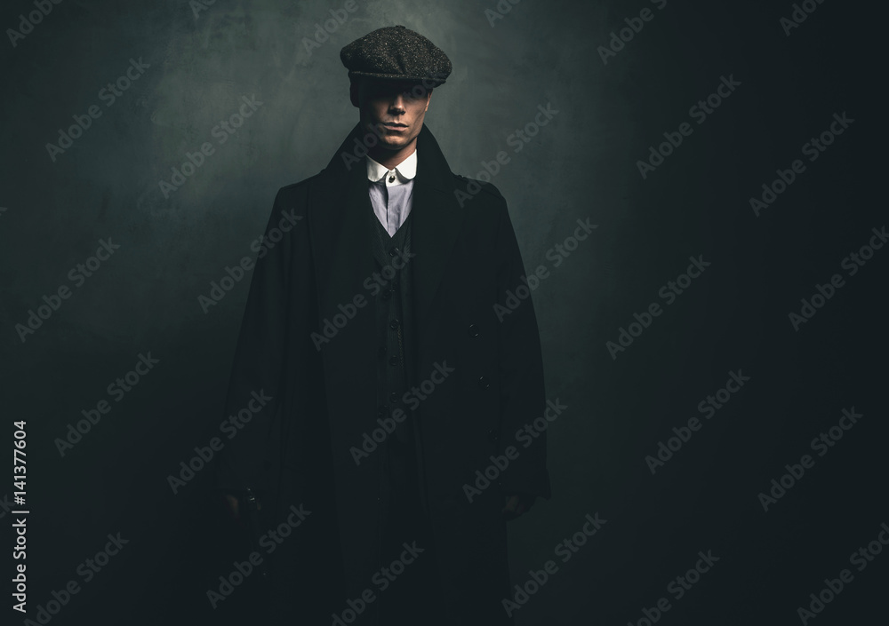 Mysterious retro 1920s english gangster with flat cap and black coat.