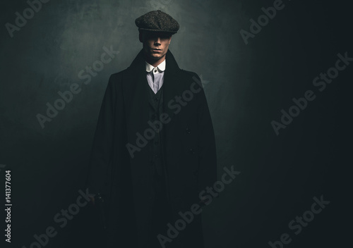 Mysterious retro 1920s english gangster with flat cap and black coat.