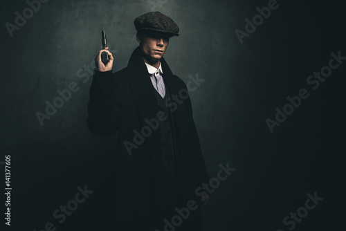 Schilderij op canvas Dangerous retro 1920s english gangster standing with gun.