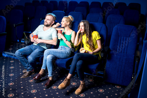 Happy friends watching film sitting together with popcorn in the cinema