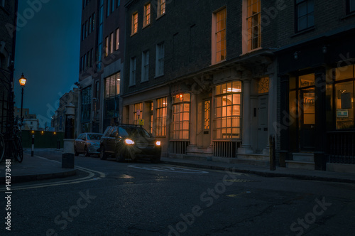 Gloomy street at night in London, UK with car headlights creating a perilous and haunting atmosphere