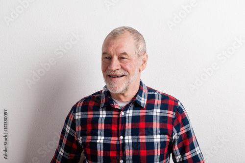 Senior man in checked shirt smiling, studio shot against white w