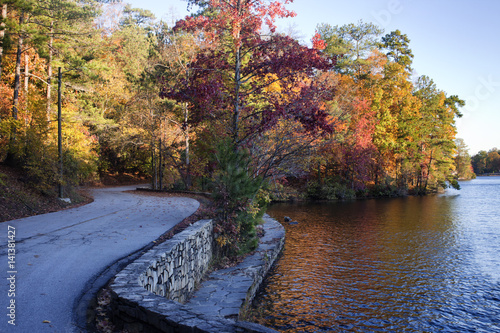 Curvy road beside lake and rock wall lined path. Colorful foliage and reflection on water.