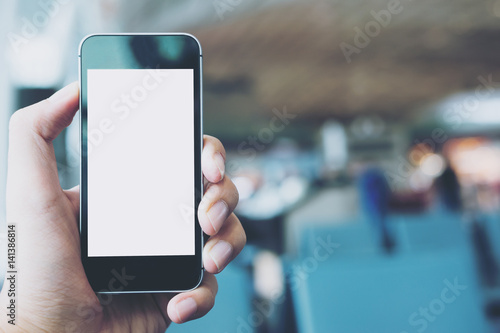 Mockup image of hand holding black mobile phone with blank white screen in airport background