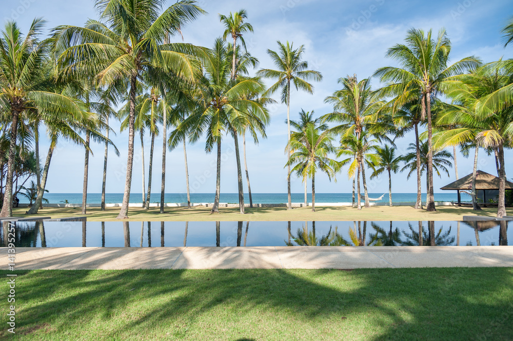 Swimming pool with coconut tree and sea background, reflection of coconut trees and white cloud and blue sky on the swimming pool at the beach Swimming pool with coconut tree and sea background, reflection of coconut trees and white cloud and blue sky on the swimming pool at the beach