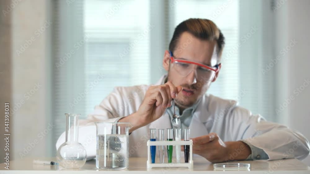 the substance foams and flows out of the tube. the chemist pours the powder into the vial of liquid. the substance foams and flows out of the tube. It wearing goggles. the substance foams and flows out of the tube. the chemist pours the powder into the vial of liquid. the substance foams and flows out of the tube. It wearing goggles.