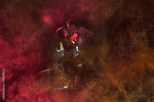 Young caucasian couple dancing tango in a burning room . Red backlight, low key image. 
