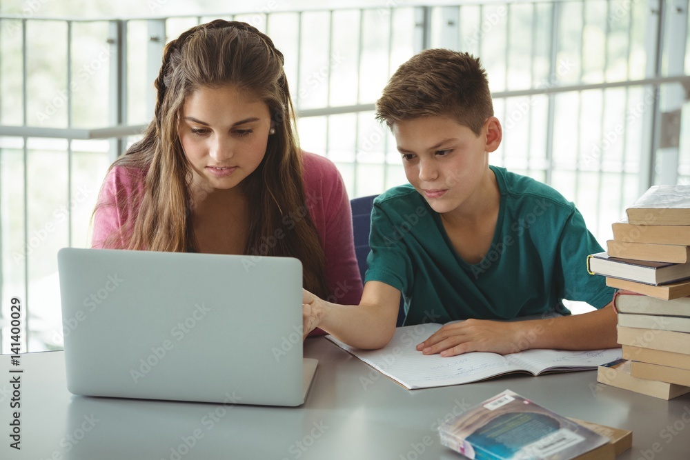School kids using laptop in library School kids using laptop in library