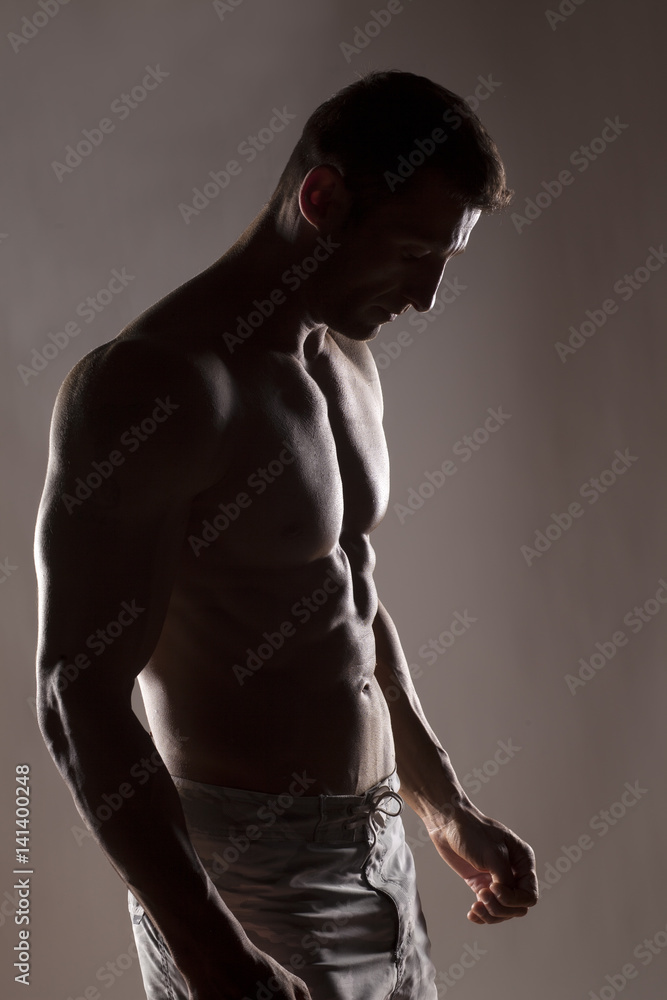 silhouette of half-naked handsome and muscular young man posing on a gray background