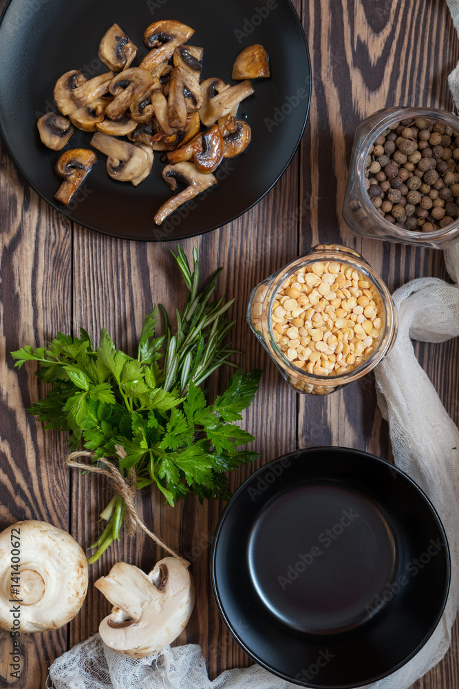 Fried mushrooms in black plate. Dried pea, pepper in glass jars. Fresh parsley and rosemary. Dark wooden table. Toned. Fried mushrooms in black plate. Dried pea, pepper in glass jars. Fresh parsley and rosemary. Dark wooden table. Toned.