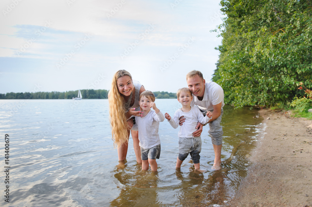 Happy family - father, mother, two sons on the beach with their feet in the water at sunset Happy family - father, mother, two sons on the beach with their feet in the water at sunset