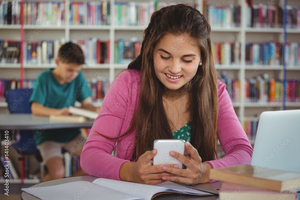 Smiling schoolgirl using mobile phone in library Smiling schoolgirl using mobile phone in library