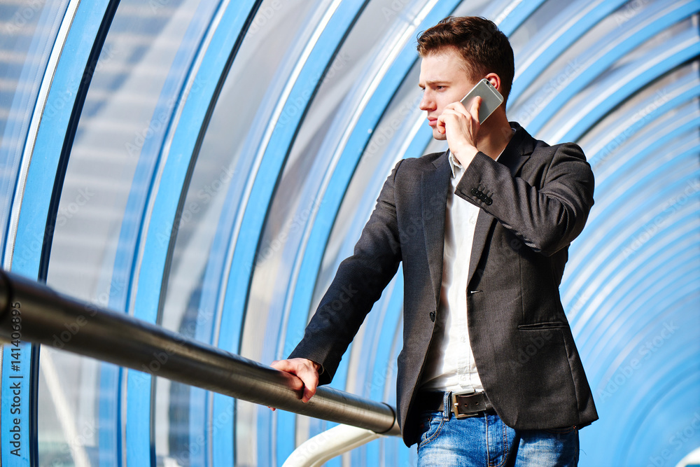 Man in suit talking on mobile phone and holds the railing in glass transition Man in suit talking on mobile phone and holds the railing in glass transition